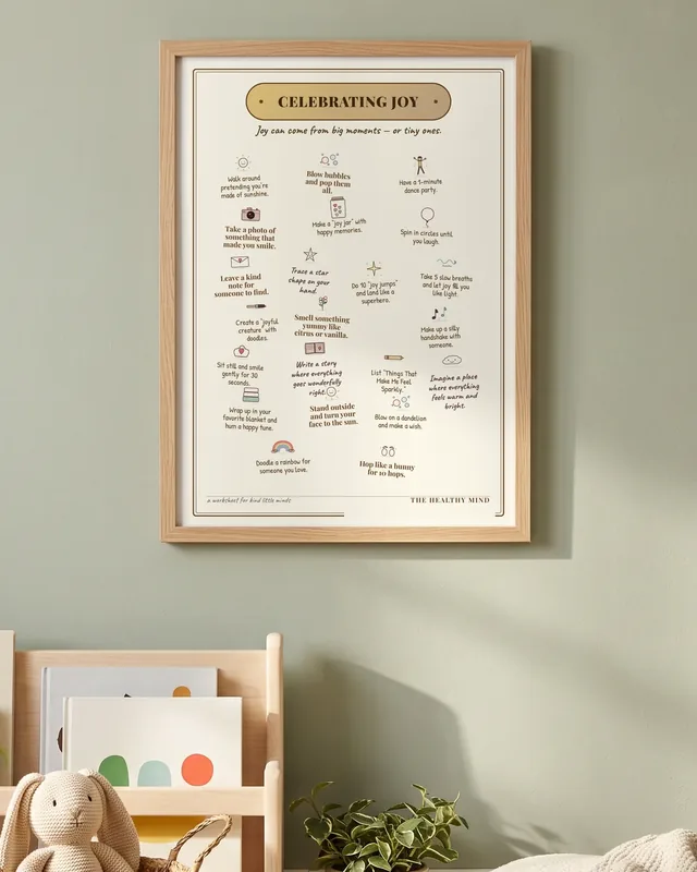 The Celebrating Joy coping skills poster in a light oak frame, above a children's book shelf with a knitted bunny.